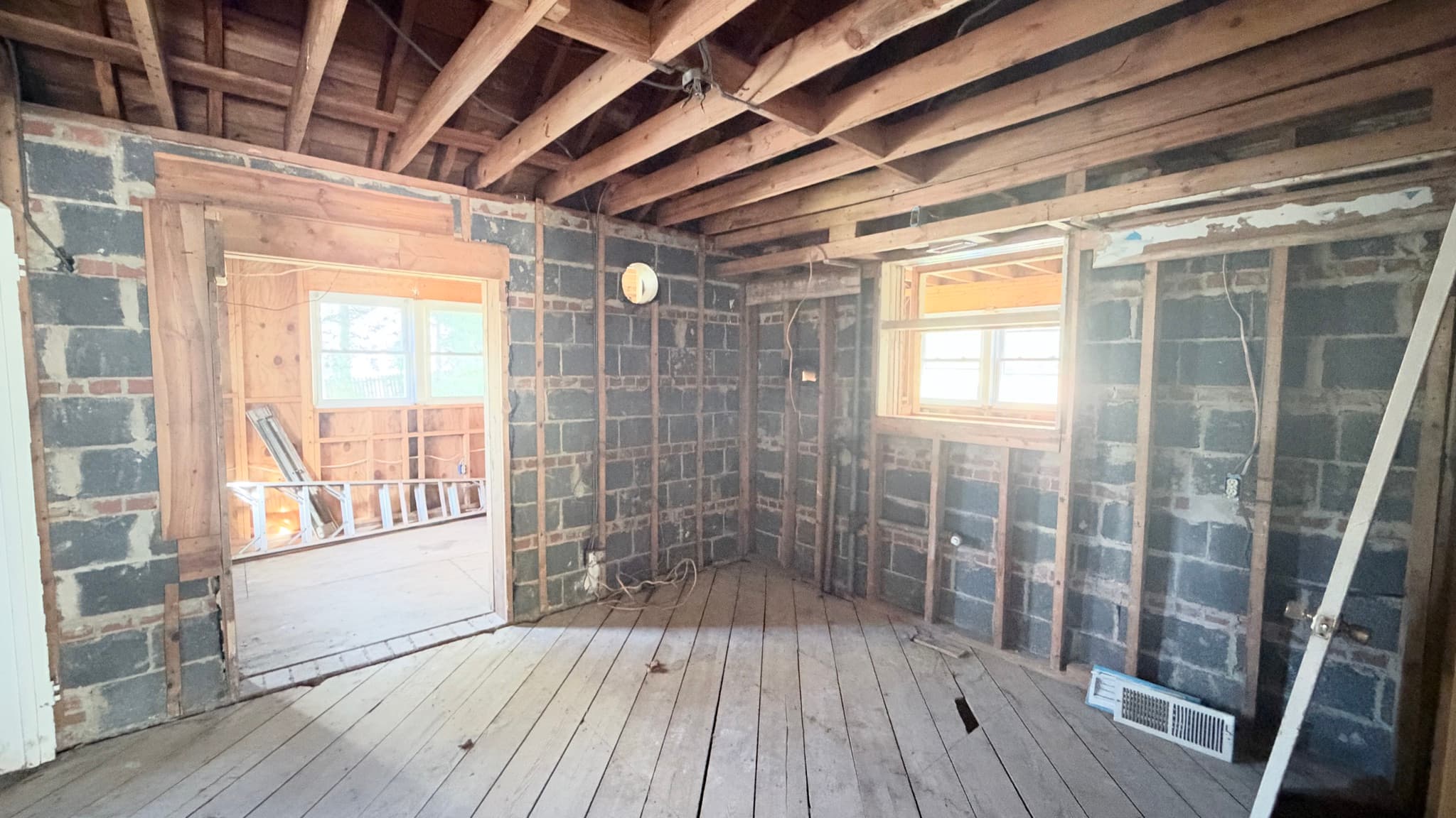 Main-level room stripped to the block walls, kitchen addition through the doorway