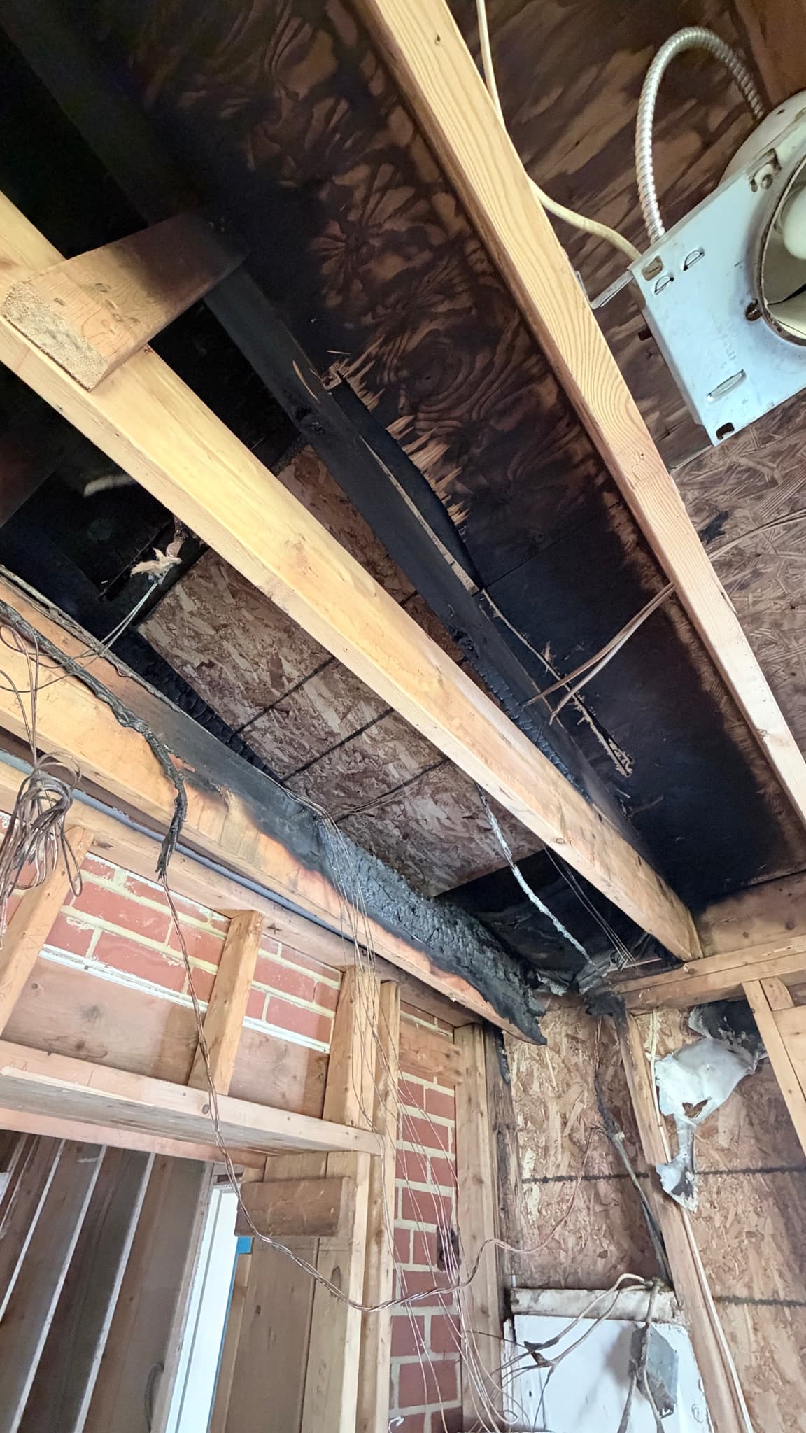 Fire damage in the kitchen addition — charred roof framing and sheathing above the brick wall
