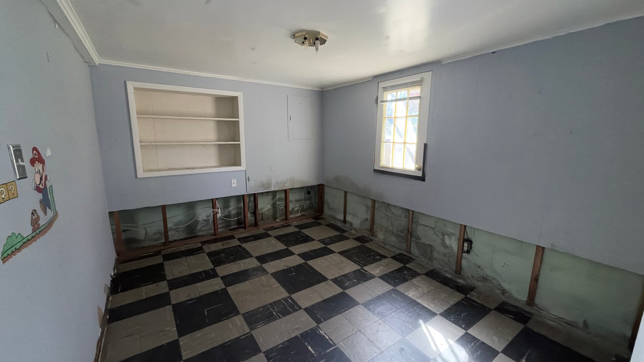 Lower-level room with built-in shelves, lower section of drywall removed