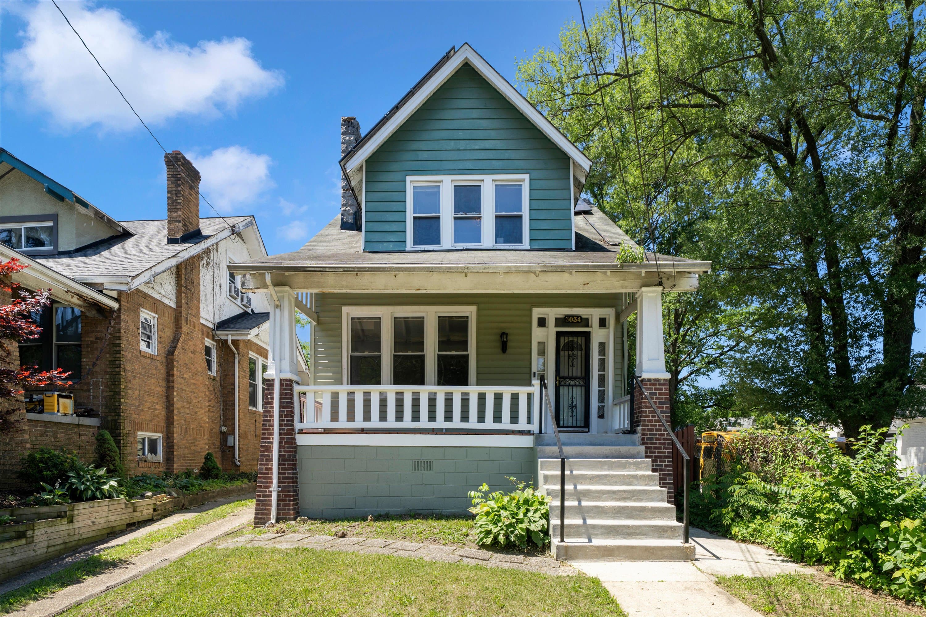 Teal-blue Craftsman front exterior of 3034 South Dakota Ave NE, a single-family home in Woodridge, Washington DC, with covered porch and mature trees